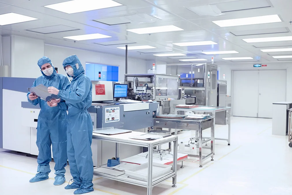 Technicians in cleanroom suits reviewing documents inside a high-tech pharmaceutical or semiconductor manufacturing facility.