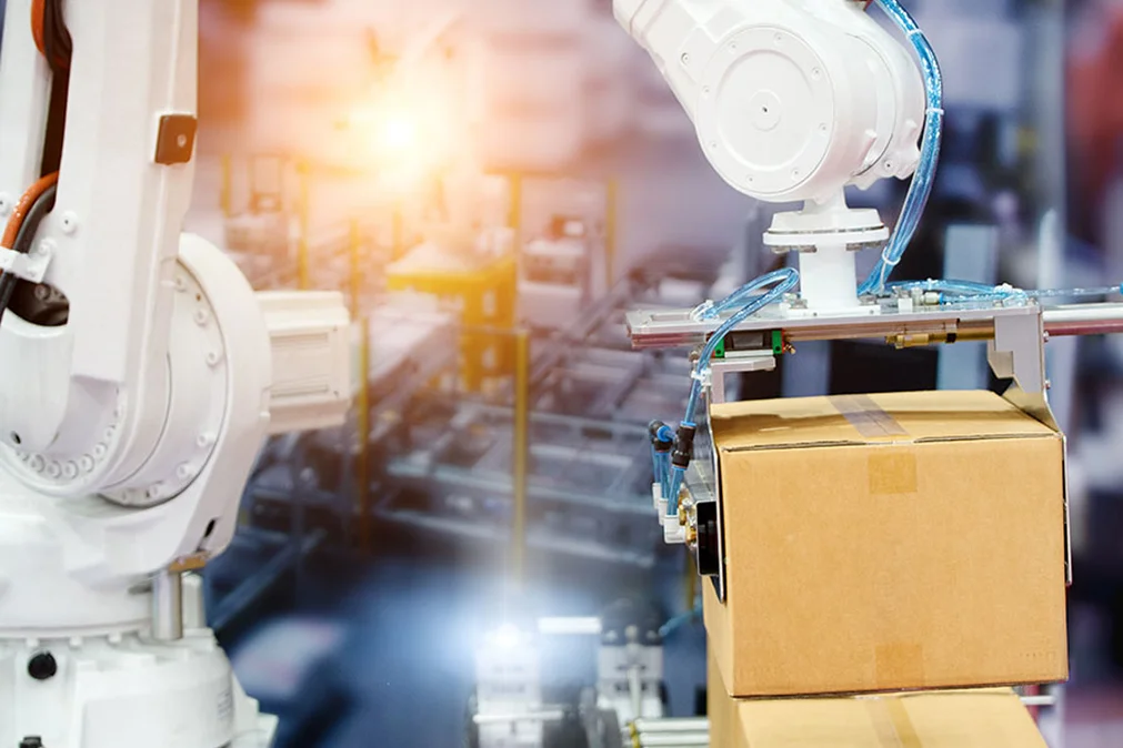 Automated robotic arm placing a cardboard box on a conveyor in a modern warehouse or manufacturing facility.