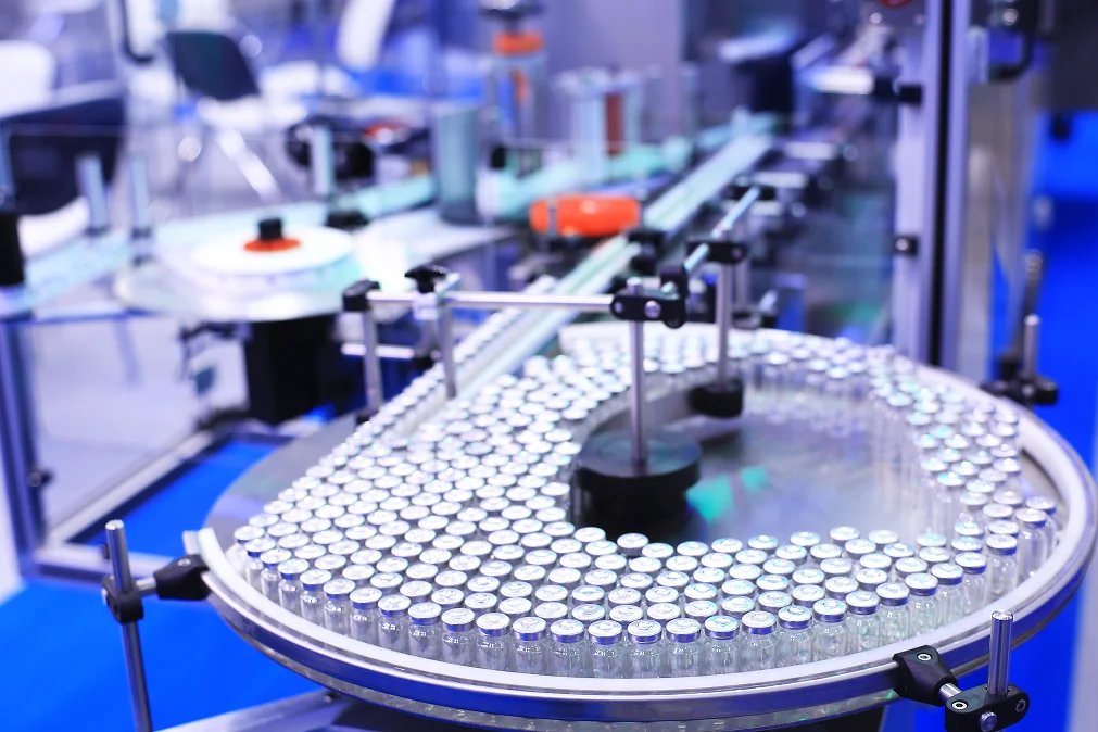 Close-up view of an automated pharmaceutical production line with glass vials being transported on a circular conveyor system.